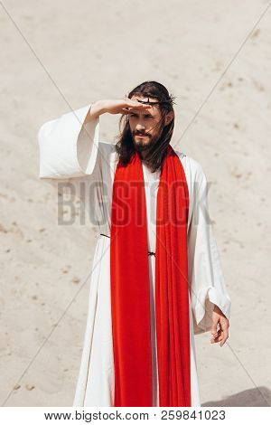 Jesus In Robe, Red Sash And Crown Of Thorns Looking Away In Desert