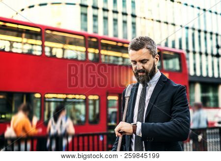 Hipster Businessman Waiting For The Bus In London, Checking The Time.