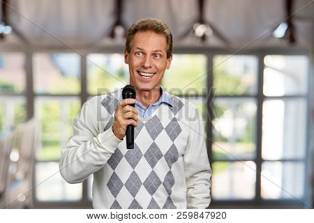 Happy Smiling Man Holding Microphone. Cheerful Middle-aged Man With Microphone On Abstract Window Ba