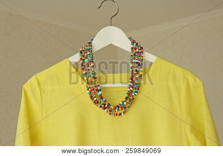 Bright Beads Of Murano Glass Hang On The Background Of A Yellow Summer Dress. Summer Jewelry, Summer