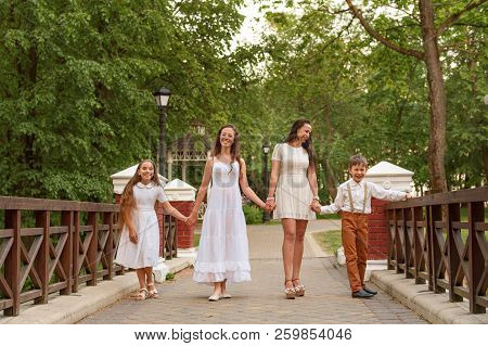 Young Mother With Children In White Dresses Walking Along The Bridge Holding Hands And Laughing Smil