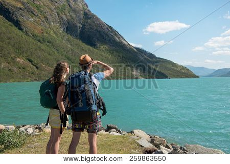 Hikers With Backpacks Looking At Gjende Lake In Jotunheimen National Park, Norway