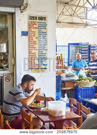 Bodrum, Turkey - July 6, 2018. A citizen eating in a Turkish tavern of Bodrum market, Kapali Pazar Yeri, and others shopping vegetables in background. Mugla Province, Turkey.