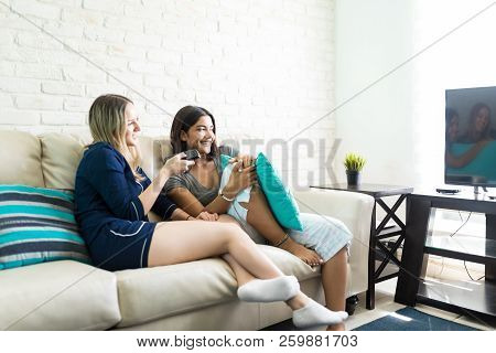 Multiethnic Roommates Watching Television While Sitting On Couch In Living Room