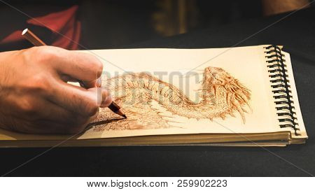 Dozza, Italy, 23 Sep 2018 - An Illustrator Hand Is Drawing A Dragon On A Sketchbook Notepad