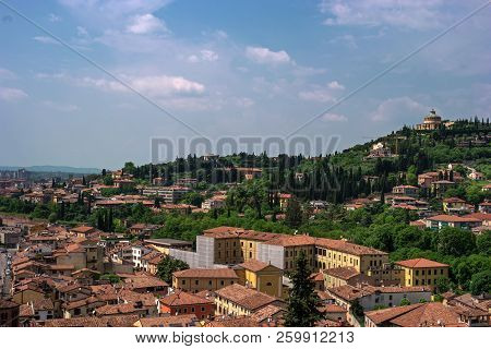 View Of The Medieval Verona, Italy. Tiled Roofs Of Houses. In The Background Santuario Della Madonna