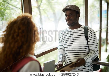 African-americn guy in casualwear talking to his groupmate of girlfriend at break in college
