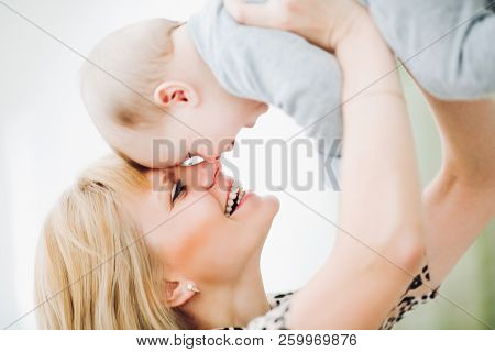 Mother Holding Her Baby Up And Toching By Noses.
