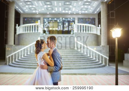 The Bride And Groom Stand On The Beautiful Porch Of The Hotel At Night