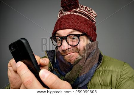 Funny Man In Glasses Anf Warm Clothes Typing Sms On Gray Background
