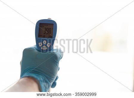 A Hand In A Blue Glove Holding An Electronic Thermometer With Indicators Of High Temperature On A Wh