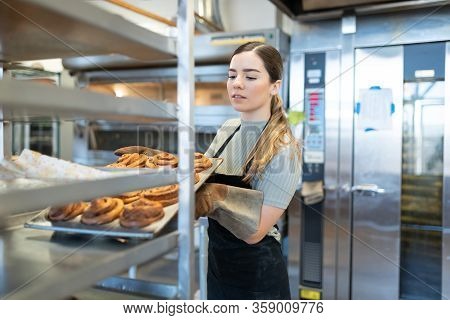 Good Looking Young Baker Setting Up A Hot Tray Of Baked Bread In A Cooling Rack In A Bakery