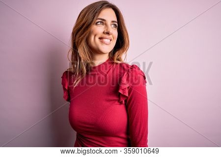 Young beautiful brunette woman wearing casual sweater stnding over pink background looking away to side with smile on face, natural expression. Laughing confident.