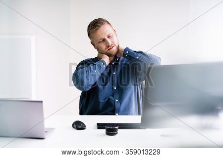 Young Businessman In Office At Desk Suffering From Neck Pain
