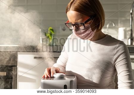 Woman In Face Protective Mask Holding In Her Hands Working Aroma Oil Humidifier In Sunny Room. Humid
