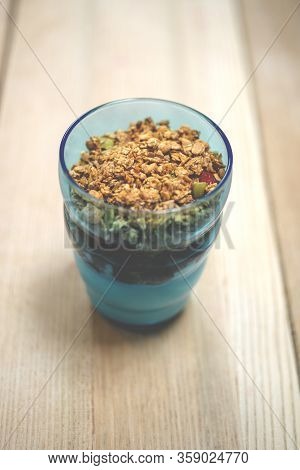 Granola Parfait In Blue Tumber On Wooden Surface