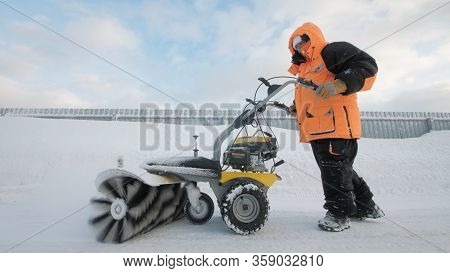 Man Cleans Snow In The Yard With A Sweeper In The Winter