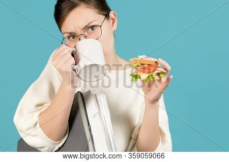 Girl Drinks Coffee And Holds A Sandwich During Working Hours. Overworked Office Worker Concept