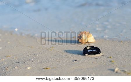 Kyiv, Ukraine - March, 18, 2020: Nikon Replacement Lens Cap On The Seashore, Among Golden Sand, Blue
