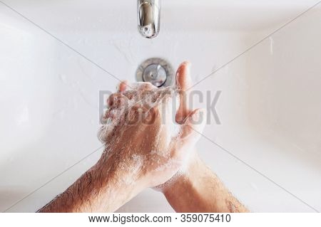 Man Cleaning His Hands Using Liquid Disinfectant Soap And Water In Bathroom.
