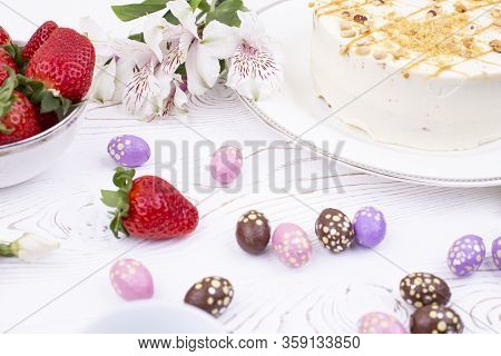 Cake Covered With White Cream And Nuts, Strawberries And Chocolate Eggs In A Multi-colored Falge.