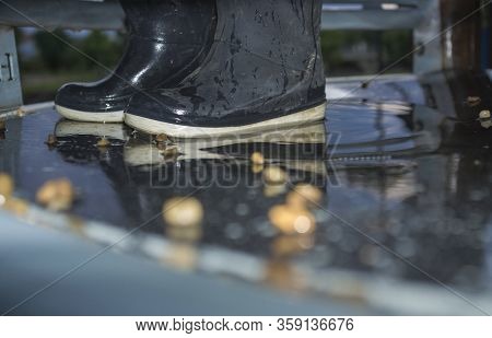 Blue Dark Child Rainboots In The Middle Of Pond Of Playground. Closeup