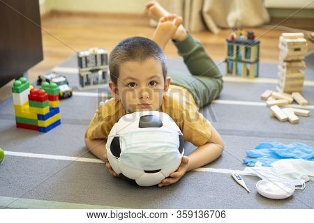 Soccer Ball In A Medical Mask. Activities At Home With Your Children During Home Coronavirus Quarant