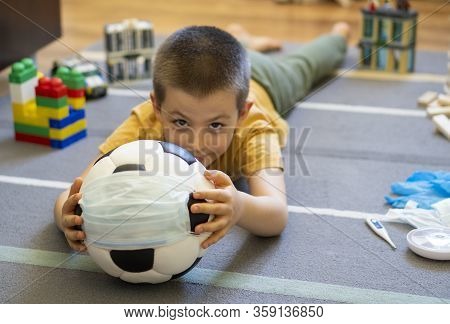 Soccer Ball In A Medical Mask. Activities At Home With Your Children During Home Coronavirus Quarant