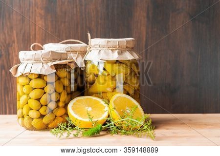 Preserved Fermented Olives And Artichokes In Oil In Glass Jars With Wild Fennel And Lemon Cut On Dar