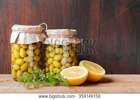 Preserved Fermented Olives In Glass Jars With Wild Fennel And Lemon Cut On Dark Wooden Background. V