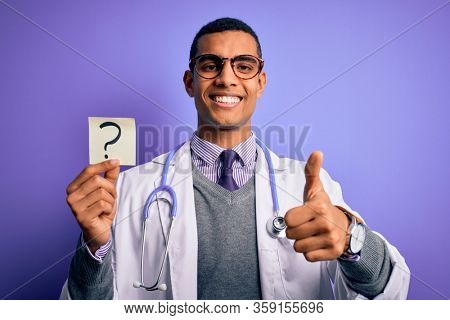 Handsome african american doctor man wearing stethoscope holding question mark reminder happy with big smile doing ok sign, thumb up with fingers, excellent sign