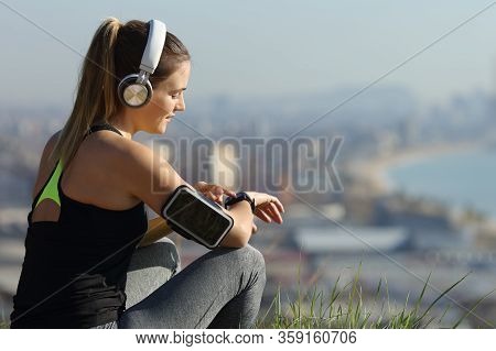 Runner Wearing Headphones Checks Music On Smartwatch Outdoors In City Outskirts