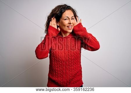 Middle age brunette woman wearing casual sweater standing over isolated white background Trying to hear both hands on ear gesture, curious for gossip. Hearing problem, deaf