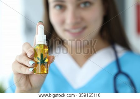 Close-up Of Female Hand Holding Bottle With Cannabinoid Oil And Marijuana Green Leaf Sign. Smiling D