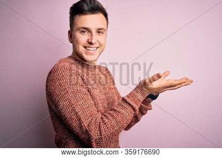 Young handsome caucasian man wearing casual winter sweater over pink isolated background pointing aside with hands open palms showing copy space, presenting advertisement smiling excited happy