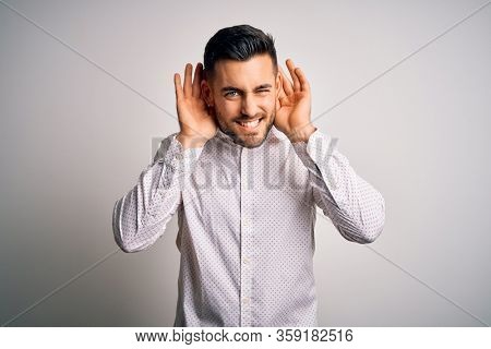 Young handsome man wearing elegant shirt standing over isolated white background Trying to hear both hands on ear gesture, curious for gossip. Hearing problem, deaf