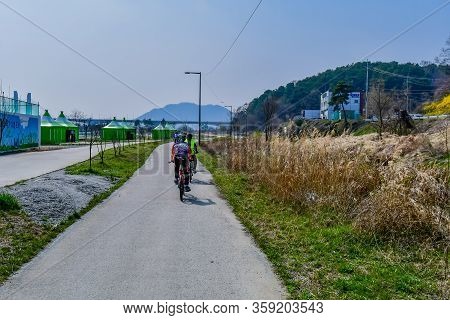 Sejong, South Korea; April 1, 2020: Unrecognizable Adults Riding Bicycles On Paved Path Through Rura