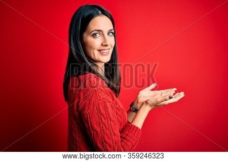 Young brunette woman with blue eyes wearing casual sweater over isolated red background pointing aside with hands open palms showing copy space, presenting advertisement smiling excited happy