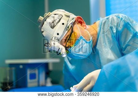 Plastic Surgeon Performing Cosmetic Surgery In Operating Room. Surgeon In Mask And Glasses Wearing S