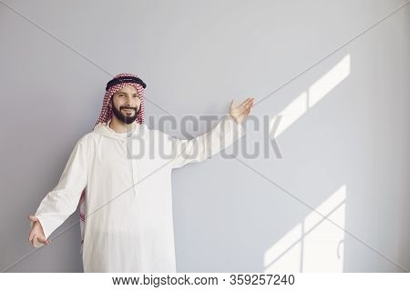 Attractive Smiling Arab Man Points His Hand To A Gray Background