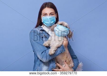 Woman Wearing Denim Jacket And Protective Medical Mask Holding Dog Pet In Face Flumask, Posing Isola