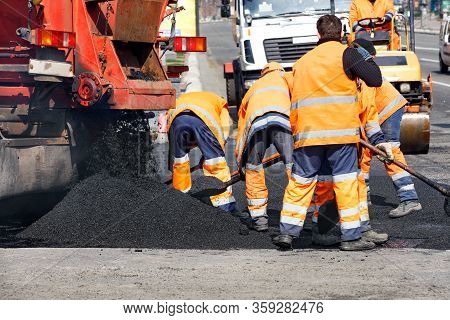 The Team Of Road Workers Updates Part Of The Road With Fresh Asphalt And Levels It With Shovels To E
