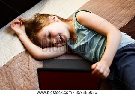 Todder Girl Laying On The Bed Looking At The Tablet And Smiling