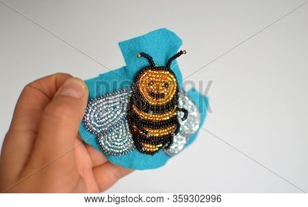 A Hand Holding Hand Made Bead Brooch Embroidered On A Piece Of Blue Felt, Shiny Golden And Silvery B