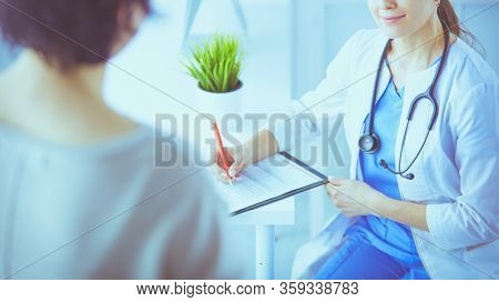 Doctor and patient discussing medical problems in a hospital consulting room. Doc filling in a patient's form