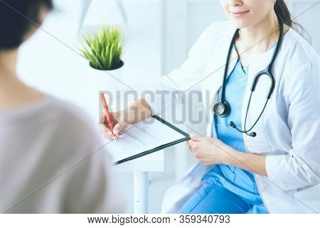 Doctor and patient discussing medical problems in a hospital consulting room. Doc filling in a patient's form