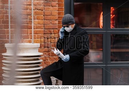 Male Entrepreneur Discusses Working Issuses Via Smartphone, Wears Protective Medical Mask And Gloves