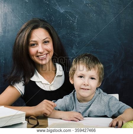 Little Cute Boy In Glasses With Young Real Teacher, Classroom Studying At Blackboard School Kido