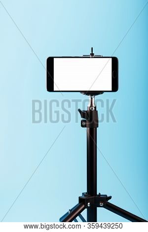Mobile Phone On A Tripod With A Clear White Display For Image And Text, Blue Isolated Background.