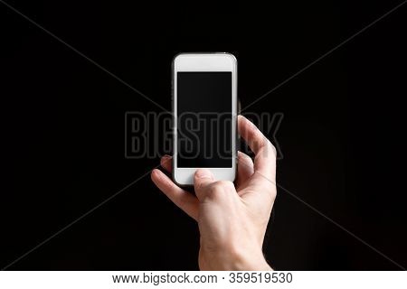 Man Holding Smartphone With Empty Screen Isolated On Black Background. Male Hands With Phone, Space 